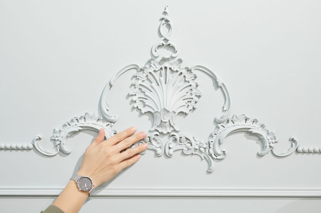 Hand of female client of studio of interior design touching ornament on wall